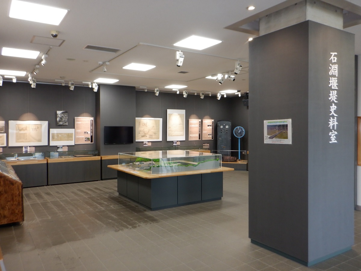 石淵堰堤史料室の様子。画像の中央に石淵ダムの模型があり、関連した展示物を収めたガラスケースが壁に設置されている。