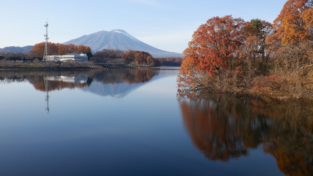 鮮やかに紅葉している木々、奥には岩手山が見える。それらが、湖面に映し出されている。
