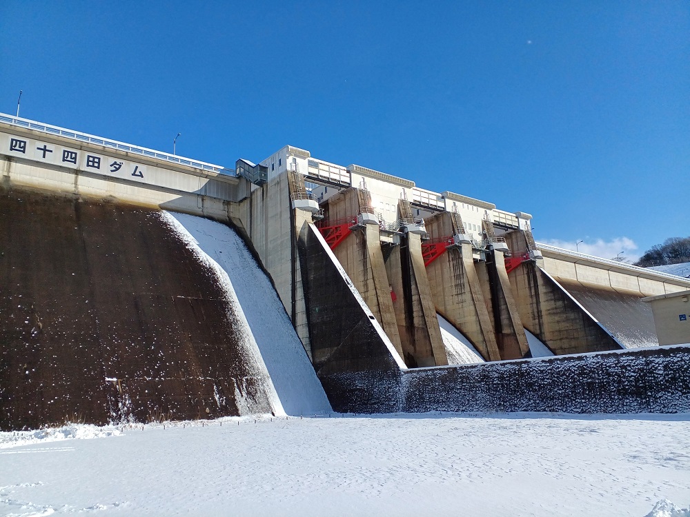雪が降った後の快晴の日、雲一つない青空と岩手山。ダム湖周辺の木々は白く雪をまとっている。湖面には雪におおわれた岩手山が鏡のように写っている。