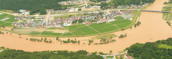 H25年7月の洪水時、堤防により守られた市街地と田畑 （大蔵村清水地区）