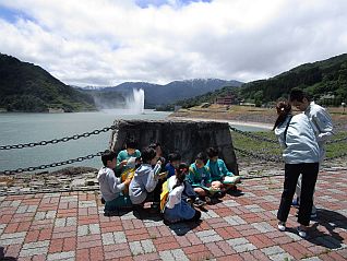 強風と噴水のしぶきから身を隠しながら説明を受ける生徒さん達