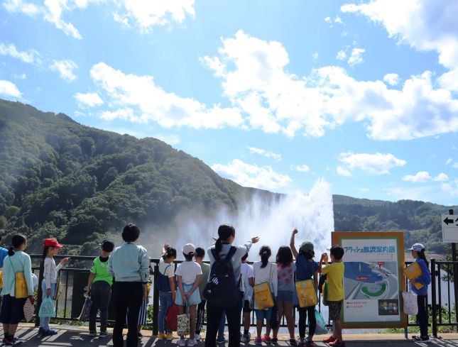 風にあおられた水しぶきを浴びながら、月山湖大噴水を眺望